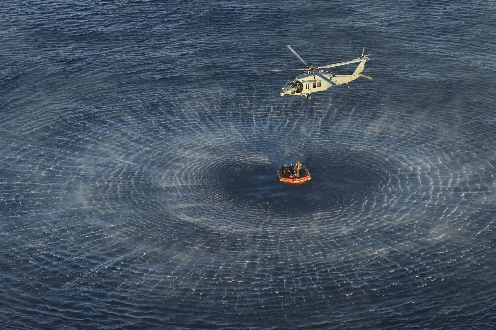 A Navy helicopter hovering over a crew raft in open ocean during a NASA Underway Recovery Test.